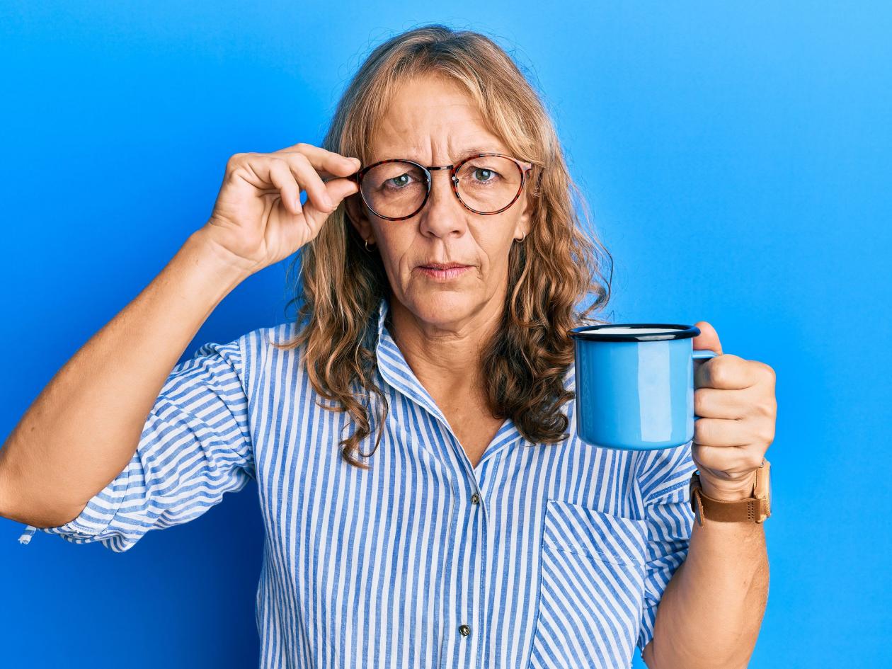 Middle age blonde woman wearing glasses and drinking a cup of coffee skeptic and nervous, frowning u