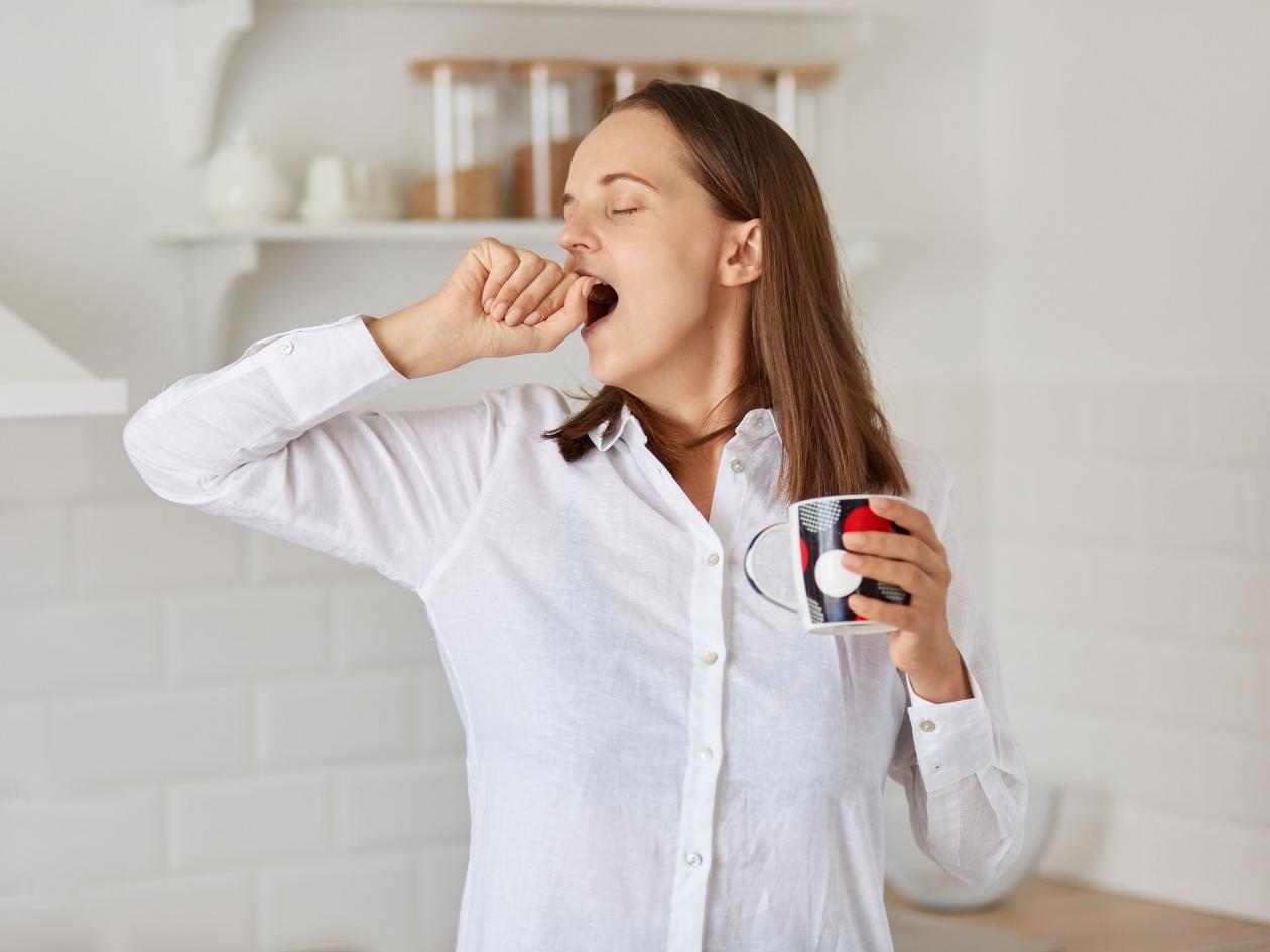 Indoor Shot Of Sleepy Happy Woman Posing In Light Kitchen, Yawning, Wakes Up Early In Morning, Yawni