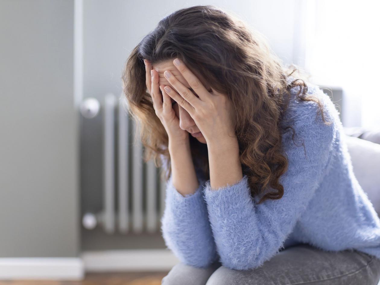 Young Depressed Woman Sitting On Sofa In Living Room. She Feeling Sad And Worried Suffering Depressi