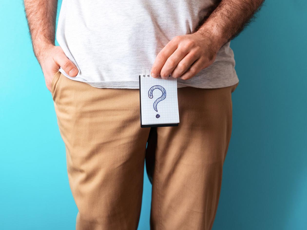 A Man In Beige Jeans Holds A Notepad With Question Mark. Close Up. Blue Background. The Concept Of A