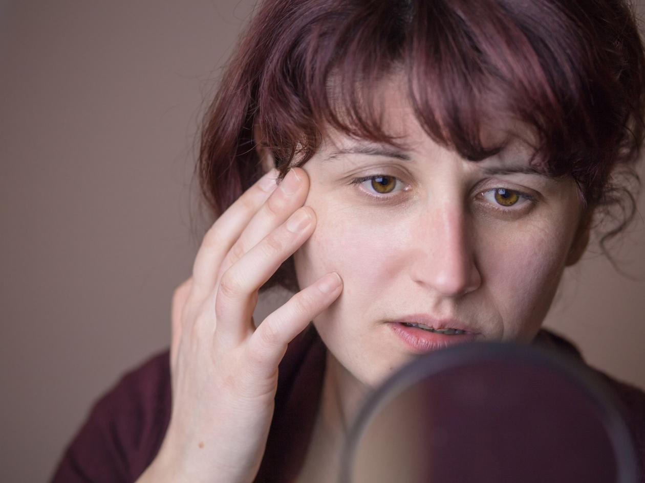 Younger Woman Looking At Her Eye Wrinkles In The Mirror. Looking Disappointed