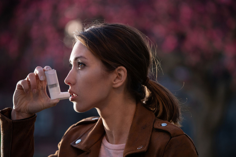 Pretty Young Woman Using Asthma Pump In Front Of Blooming Tree In Spring. Seasonal Allergy Attack