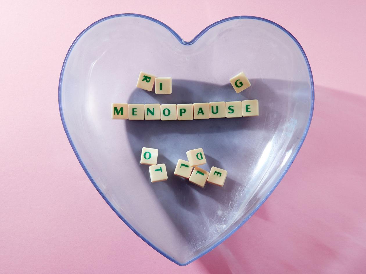 menopause word written on square block in a heart shape container. menopause text on pink  backgroun