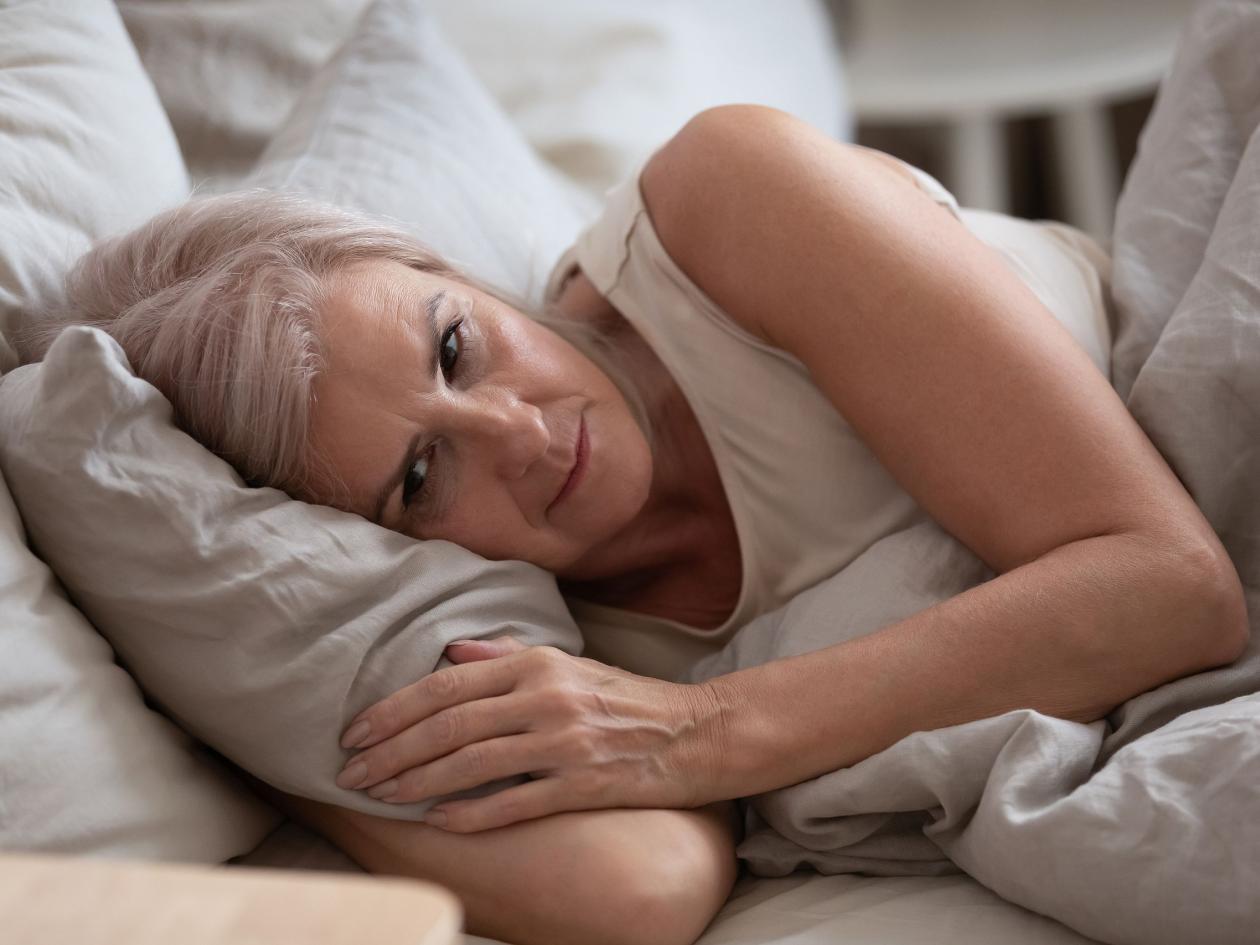 Sad Elderly Woman Lying In Bed Suffers From Insomnia