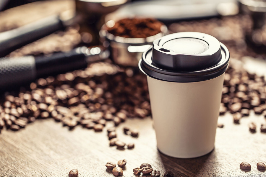 Paper Takeaway Cup With A Plastic Lid With A Coffee With Coffee Beans And Ground Coffee In The Backg